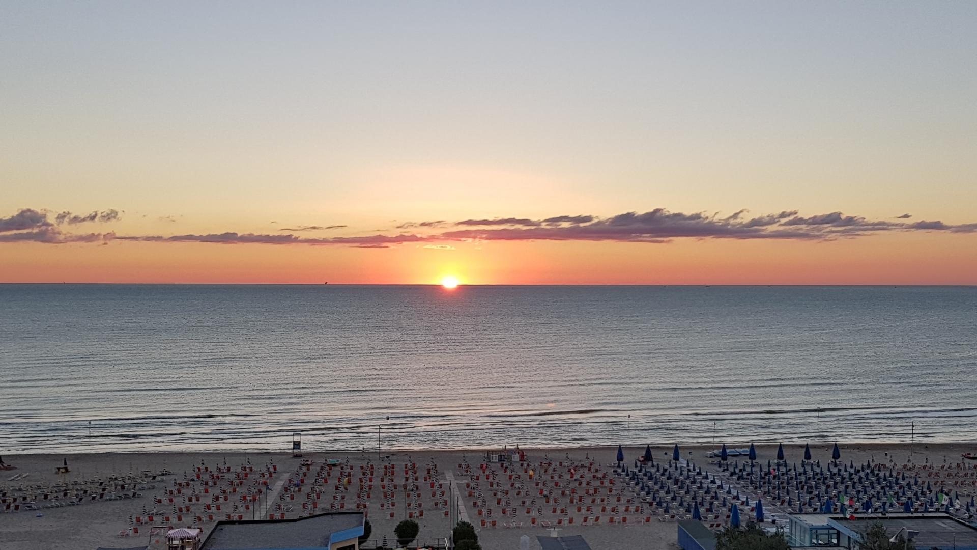 Tramonto sulla spiaggia con ombrelloni chiusi, mare calmo e cielo colorato.