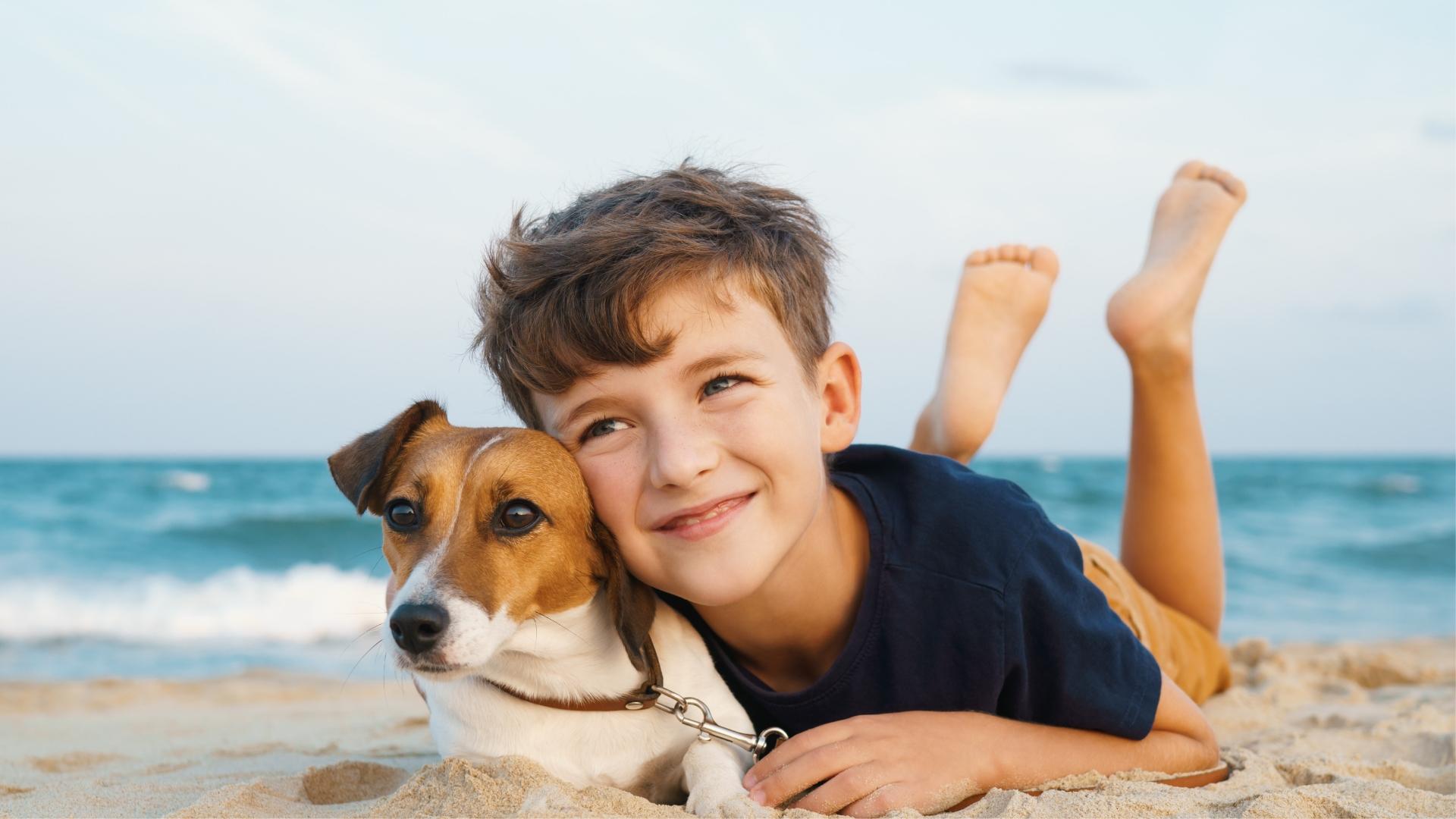 Bambino felice abbraccia il suo cane sulla spiaggia, con il mare sullo sfondo.