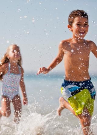 Bambini che corrono felici in spiaggia, spruzzando acqua ovunque.