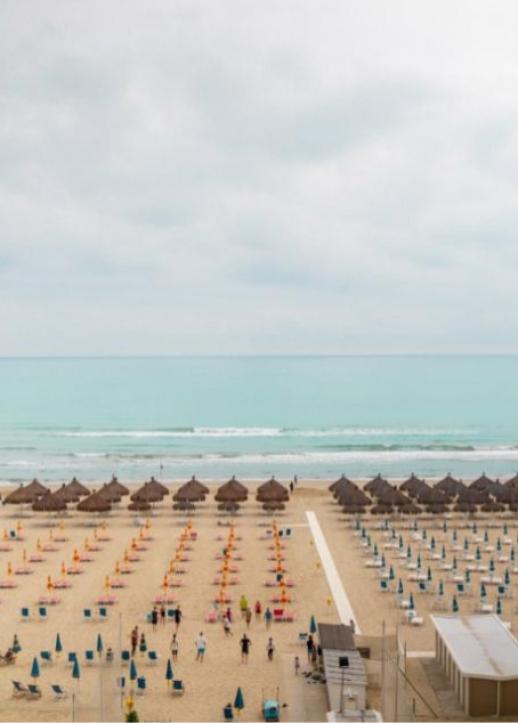 Spiaggia con ombrelloni colorati, capanne di paglia e mare calmo sotto un cielo nuvoloso.