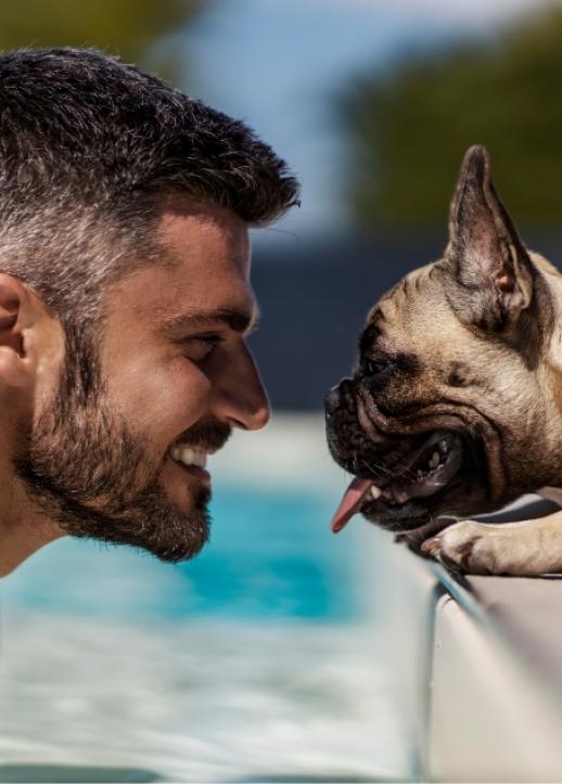 Uomo e cane si guardano sorridenti a bordo piscina in un momento di complicità.