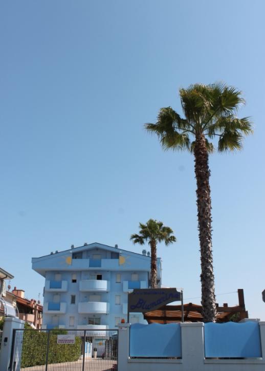 Edificio blu con palme, cielo sereno e insegna Blumarine, ingresso recintato.