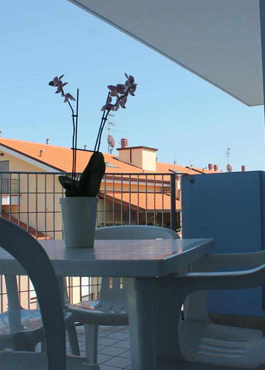 Vista dal balcone su edifici moderni e alberi, con tavolo e sedie in primo piano.