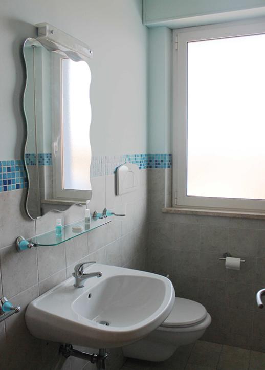 Bagno moderno con lavabo, specchio ondulato, WC e finestra grande.