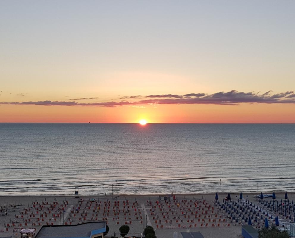 Tramonto sulla spiaggia con ombrelloni chiusi, mare calmo e cielo colorato.